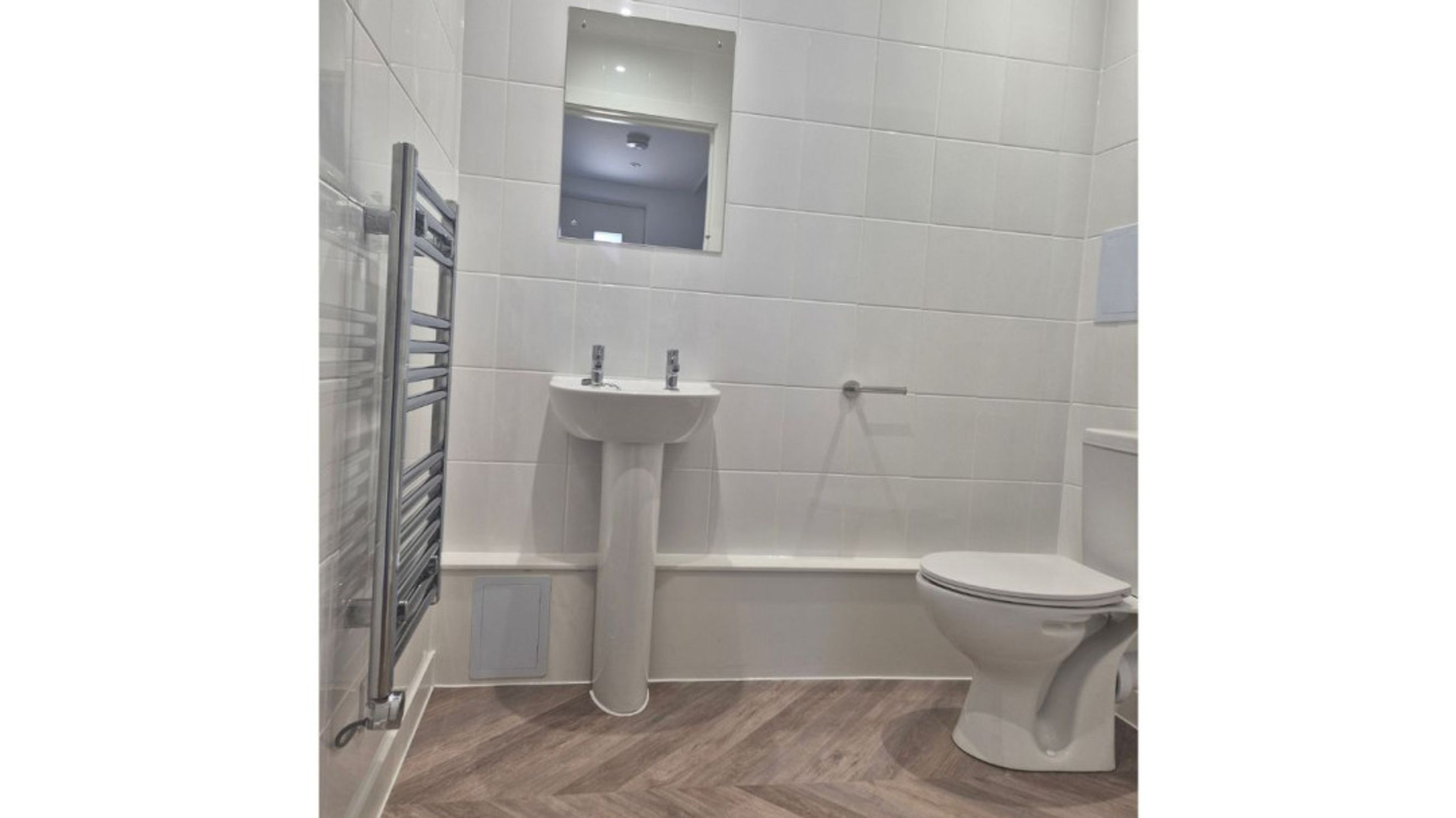A bathroom with a sink, toilet, mirror, and towel warmer.