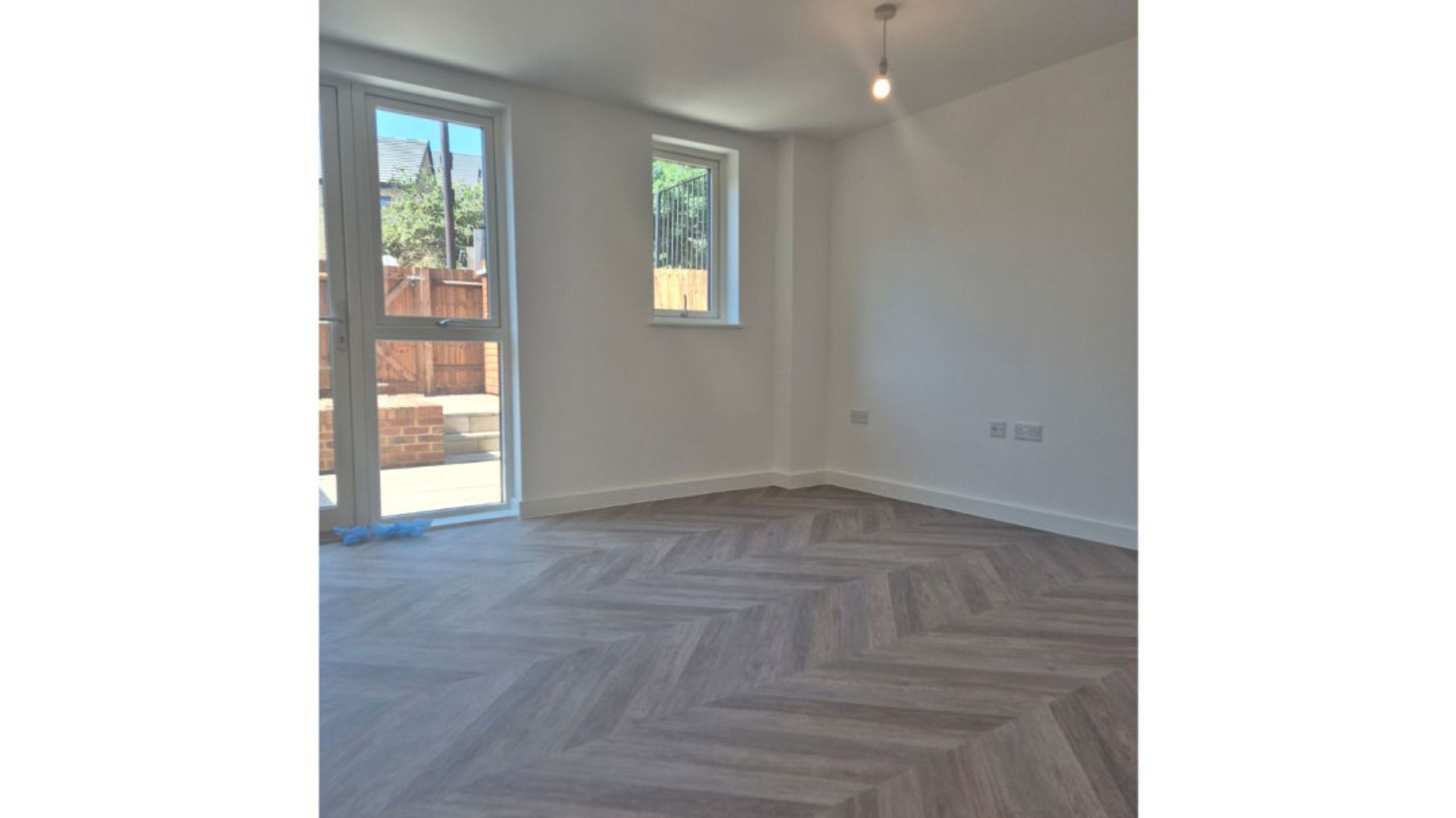 A room with a herringbone floor, a window, and glass doors leading outside.