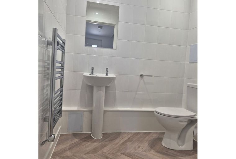 A bathroom with a sink, toilet, mirror, and towel warmer.