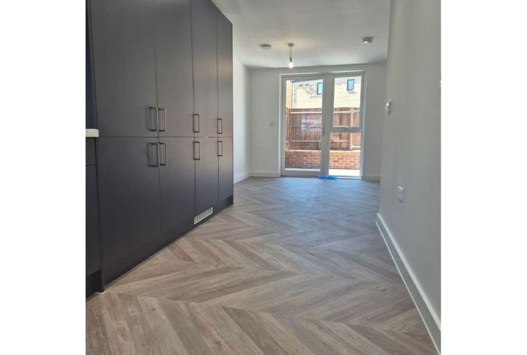 A hallway with dark cabinets and a herringbone floor leading to glass doors.