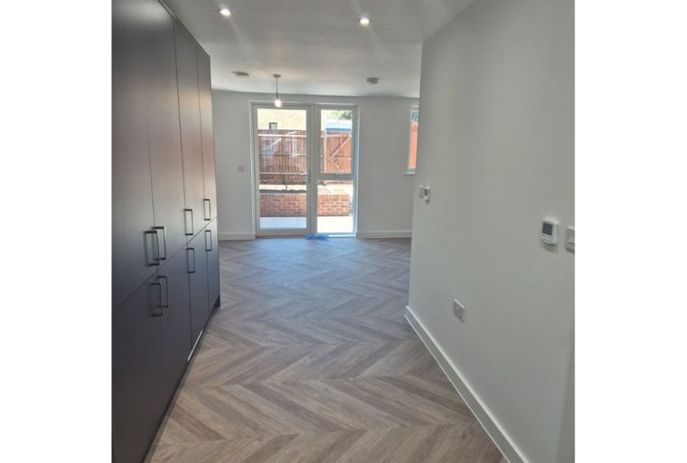 A hallway with a large dark grey wardrobe and a herringbone floor leading to a room with double glass doors.
