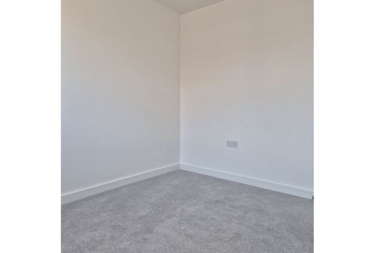A corner of a room with white walls, grey carpet, and a white electrical socket.