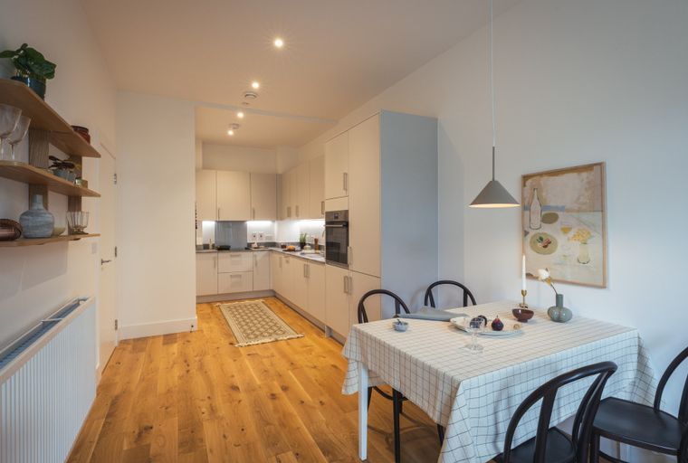 A dining area and kitchen with wooden floors and white cabinets.