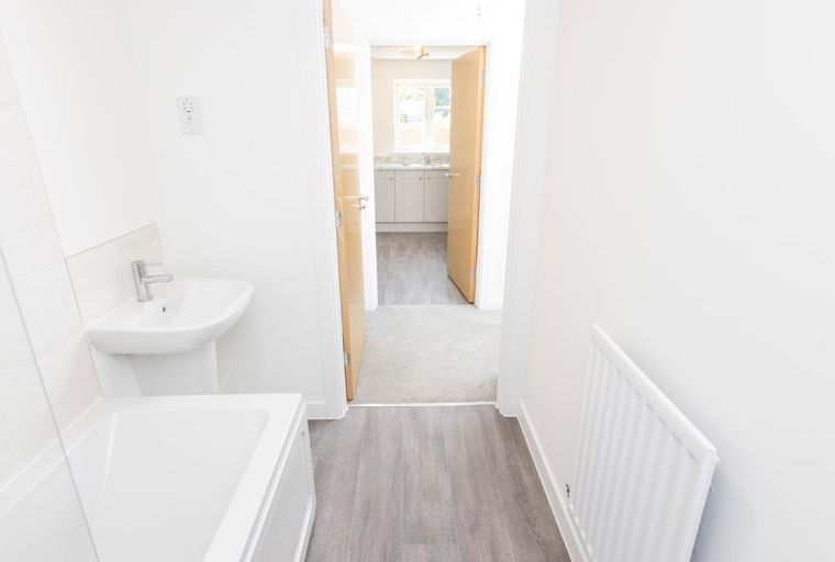 A hallway with a bathroom on the left and a kitchen visible through an open doorway.