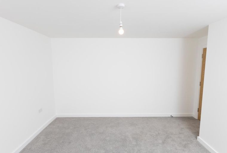 A room with white walls, grey carpet, and a pendant light.