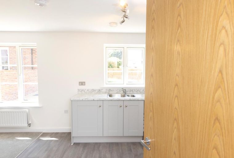 A kitchen area with a double sink, light grey cabinets, and windows.
