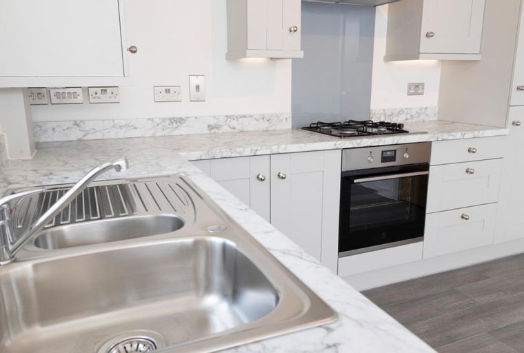 A kitchen with a double sink, faucet, marble countertop, oven, and gas hob.