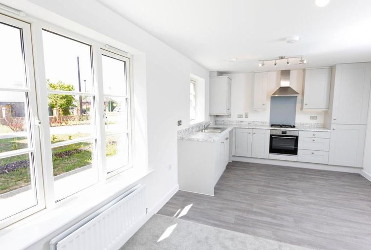 A modern kitchen with grey cabinets, a built-in oven, and a double sink, illuminated by natural light from large windows.