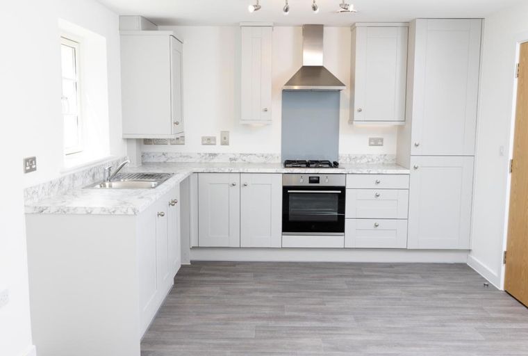 A modern kitchen with light gray cabinets, marble countertops, and stainless steel appliances.