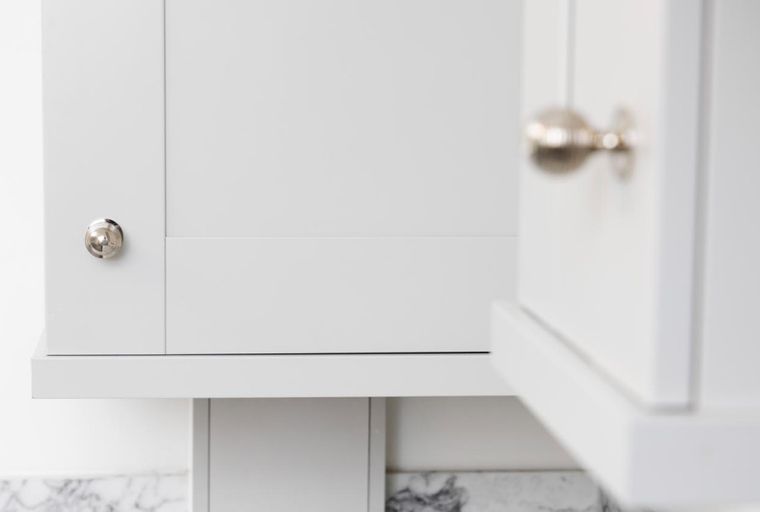 A close-up of white kitchen cabinets with silver knobs.