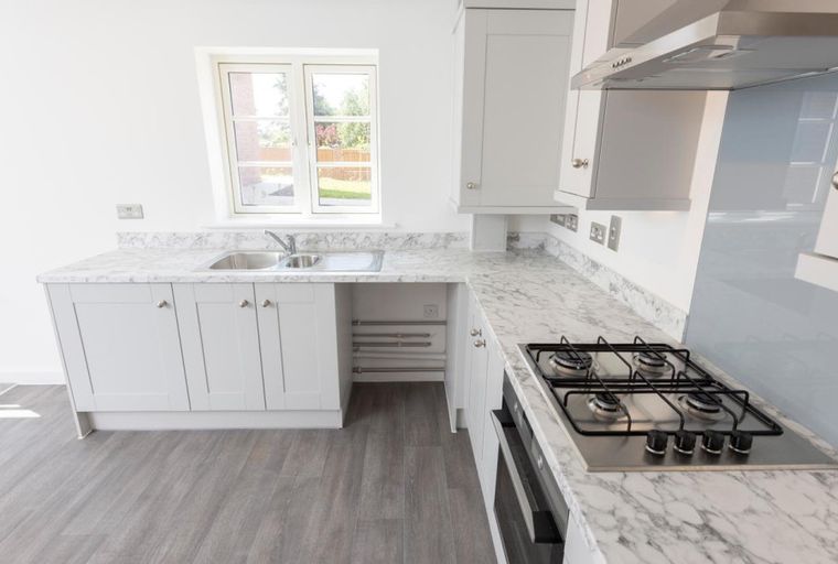 A modern kitchen with white cabinets, marble countertops, a sink, and a gas hob.