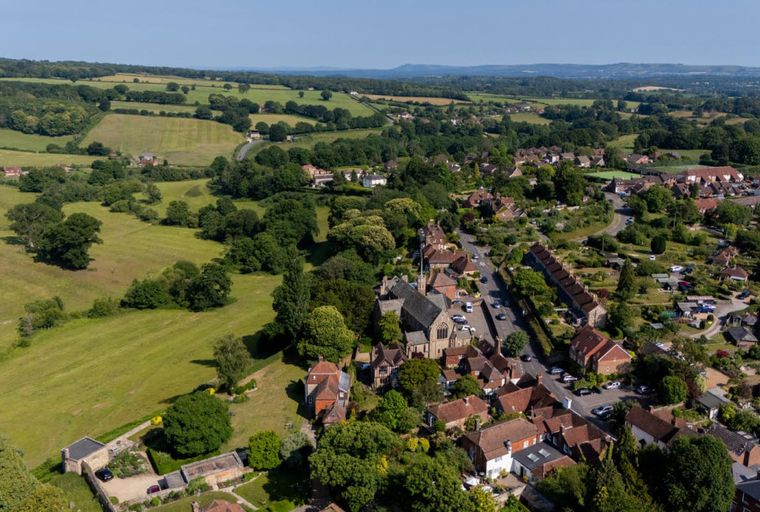 An aerial view of a village with houses, a church, and surrounding green fields.