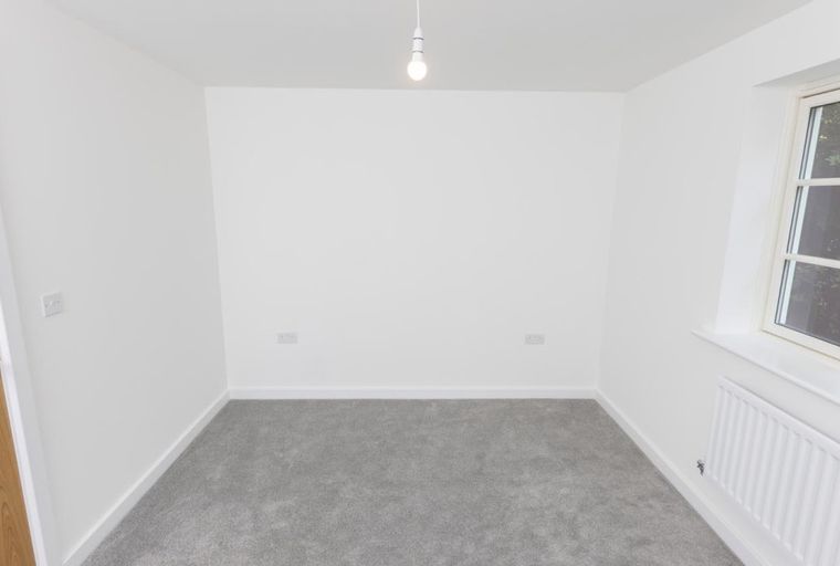 A room with grey carpet, white walls, a window, and a radiator.