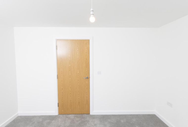 A room with a wooden door, grey carpet, and a light bulb hanging from the ceiling.