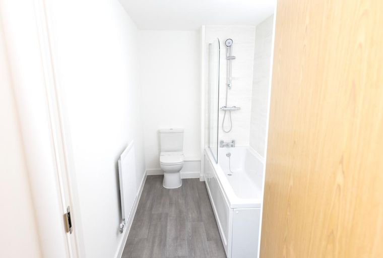 A bathroom with a bathtub, shower screen, toilet, and radiator.