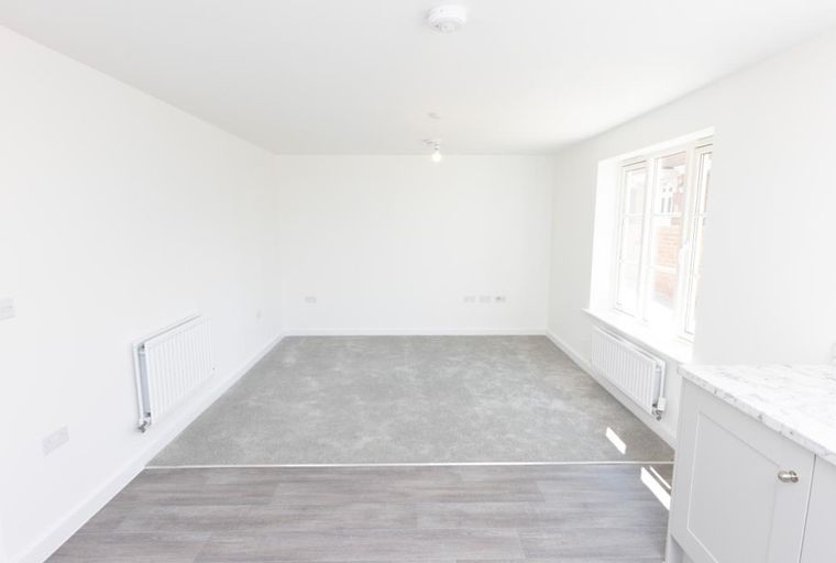 A living room with carpeted flooring, radiators, and a window.