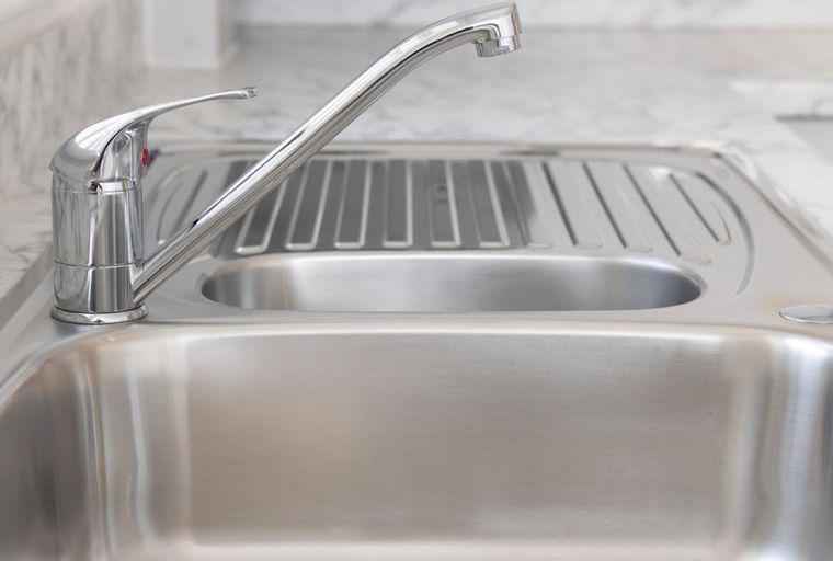 A stainless steel kitchen sink with a faucet and drainboard.