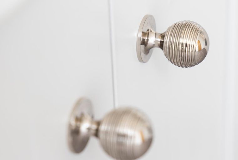 A pair of fluted, silver cabinet knobs on a white surface.