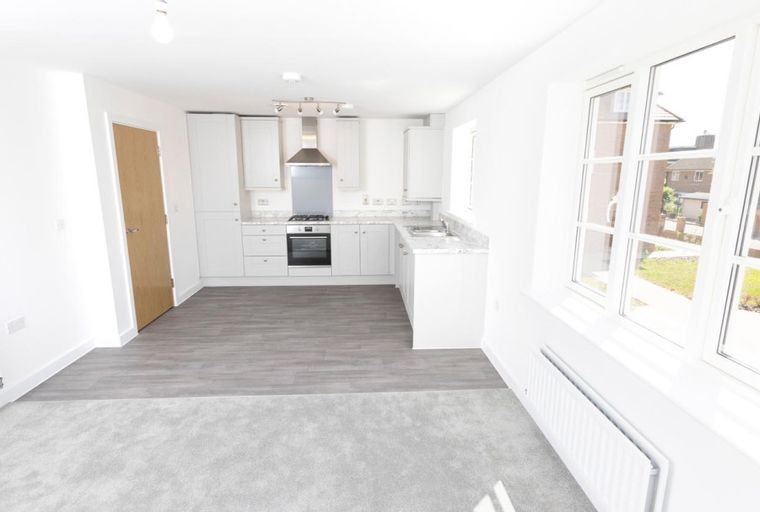 A kitchen and living area with white cabinets, grey flooring, and large windows.