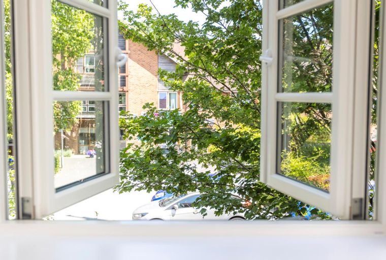 A view through an open window of trees, buildings, and a car.