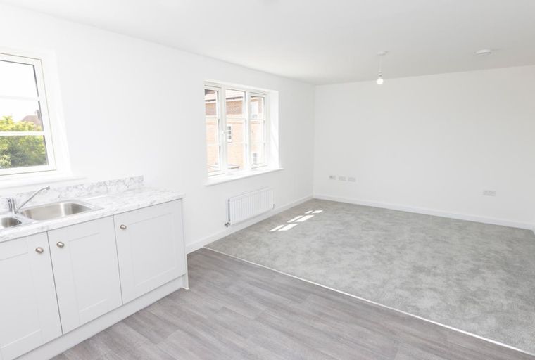 A living room with a kitchen area, a sink, windows, and carpet.
