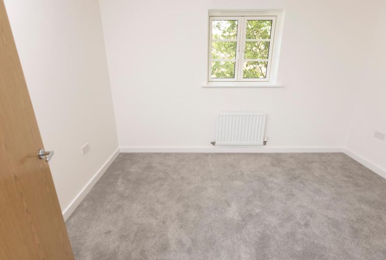 A room with a wooden door, a window, a radiator, and grey carpet.