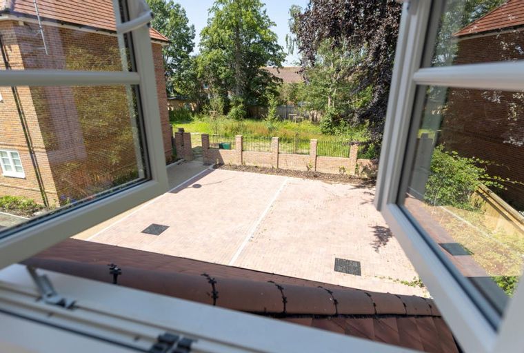 A view from an open window overlooking a paved courtyard and a garden with trees.