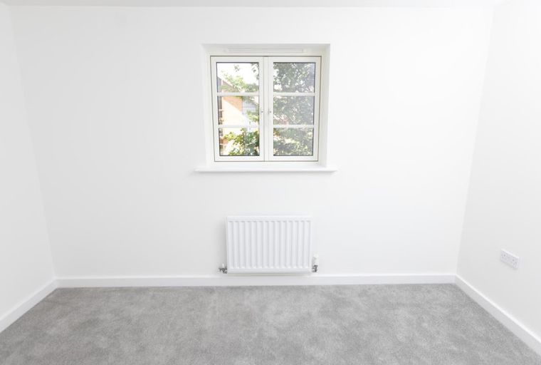 A room with a window, radiator, and grey carpet.