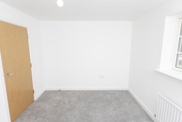 A room with a wooden door, grey carpet, and a window.