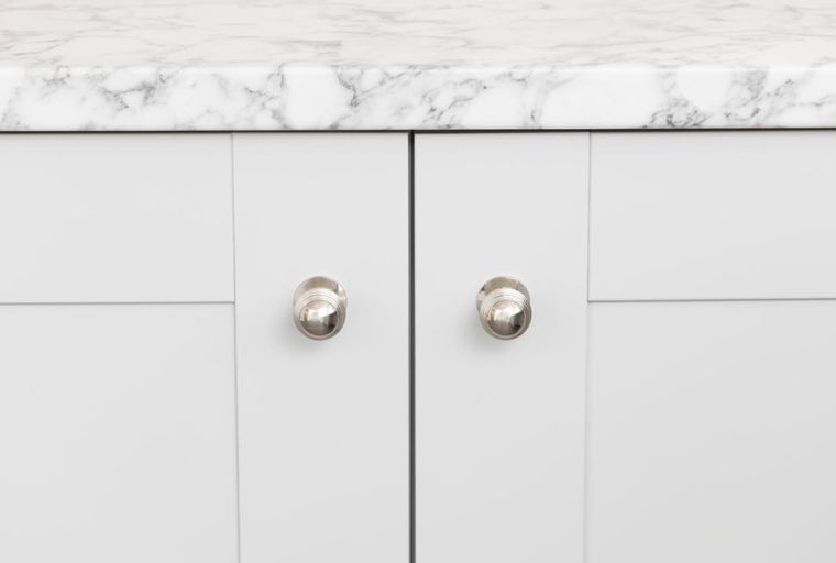 A white cabinet with a marble countertop and two silver knobs.