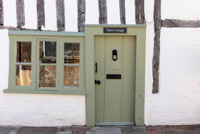 A green door and window on a whitewashed Tudor-style cottage with exposed wooden beams.