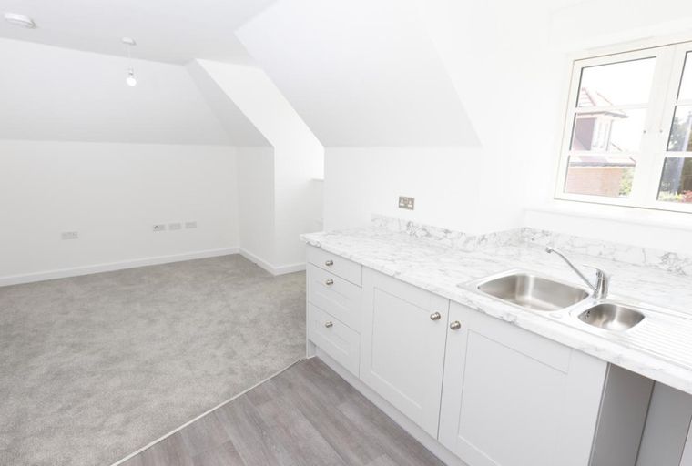 A room with a kitchenette, sink, and carpet.
