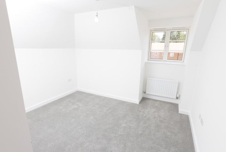 A bedroom with a grey carpet, white walls, a window, and a radiator.
