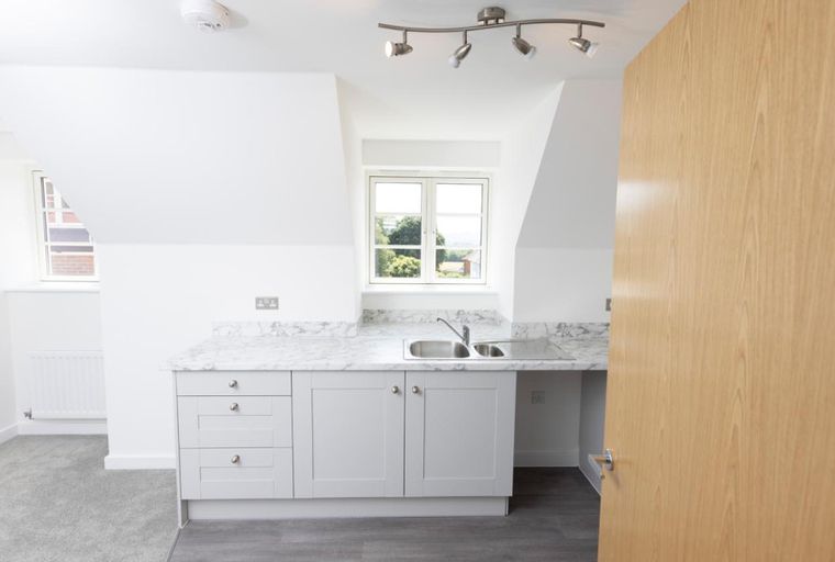 A kitchenette with a sink and cabinets in a room with a window and a door.