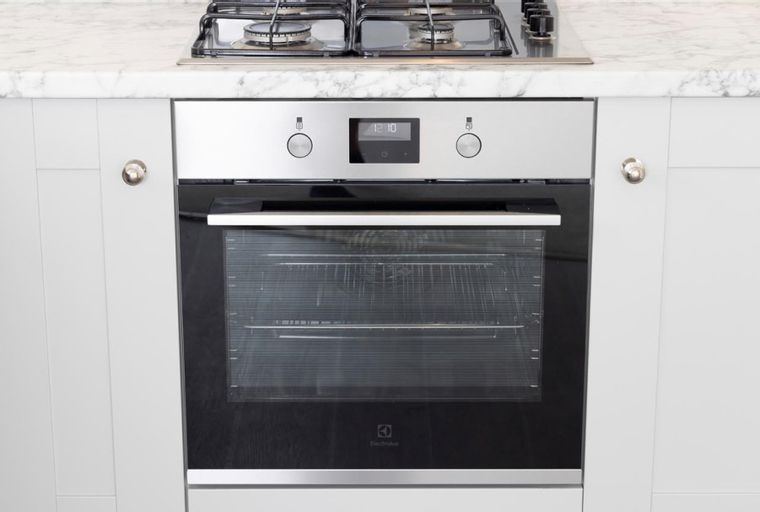 A built-in oven with a digital display and knobs, set within light gray kitchen cabinets.