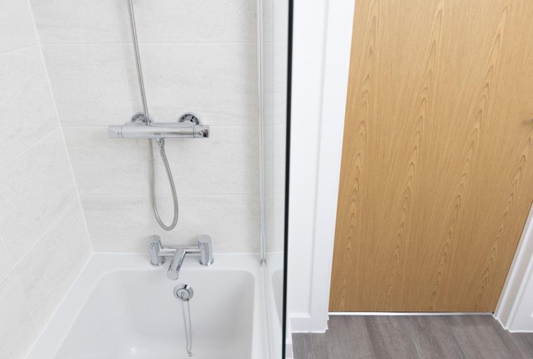 A bathtub with a shower fixture next to a wooden door.