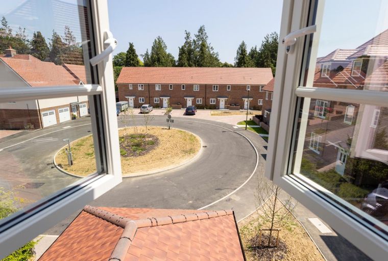 A view through an open window of a residential street with townhouses and detached homes.