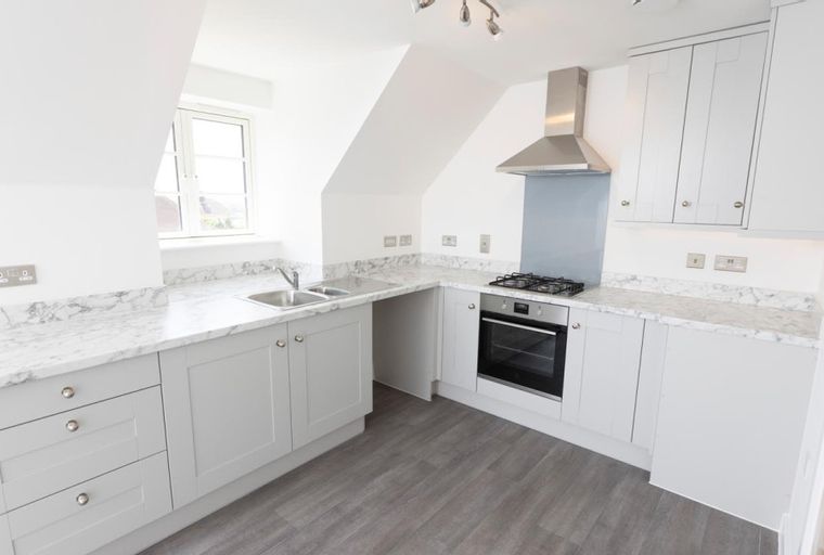 A modern kitchen with grey cabinets, marble countertops, a gas hob, and an oven.