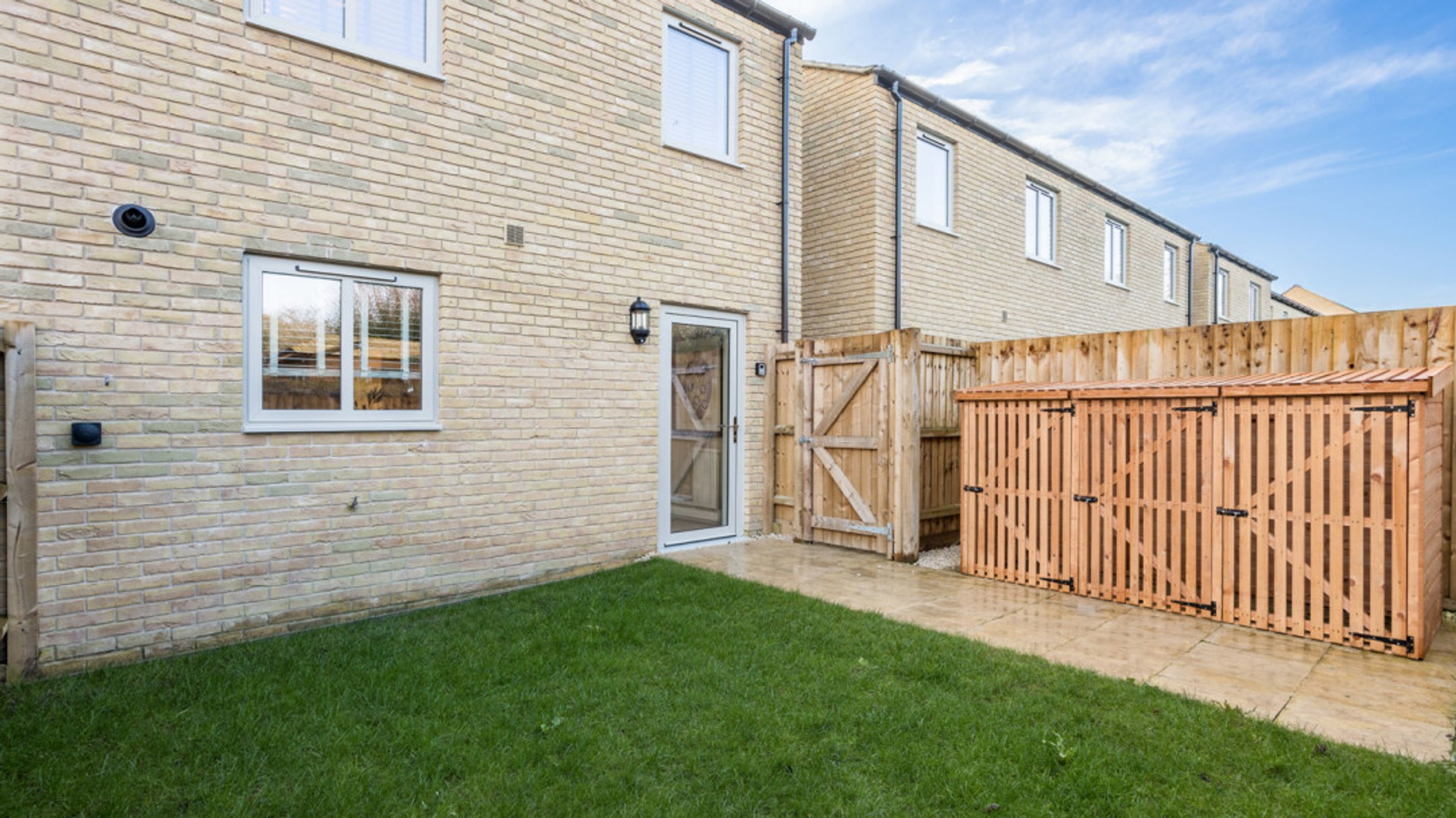 A backyard with a lawn, patio, wooden storage unit, and fence.