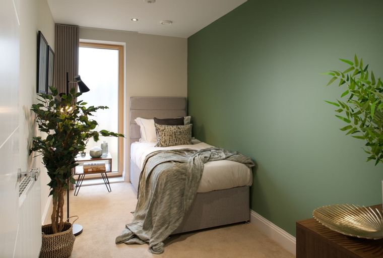 A bedroom with a single bed, a window, and a plant.