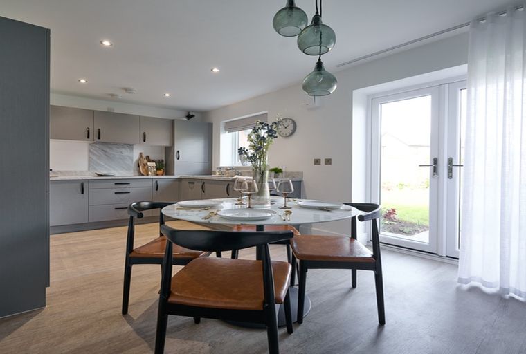 A dining area with a round table and chairs in front of a kitchen.