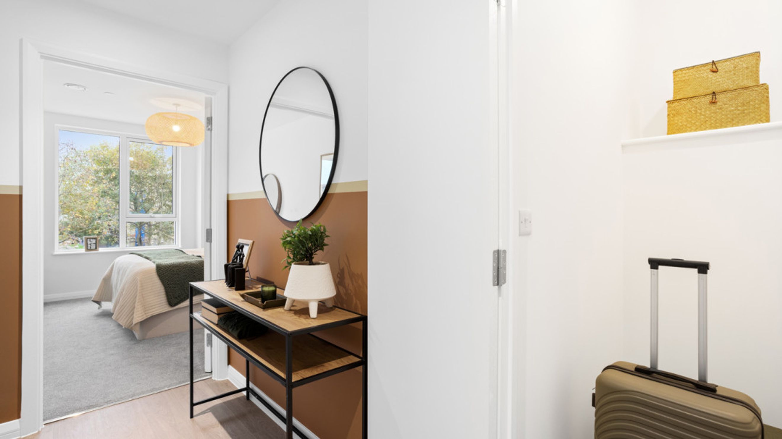A hallway with a console table and mirror leads to a bedroom with a bed and a window.