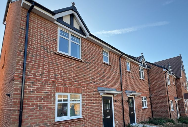 A row of brick townhouses with white windows and black doors under a blue sky.