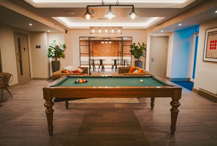 A billiard table with balls and a cue ball on a green felt surface in a room with seating areas.