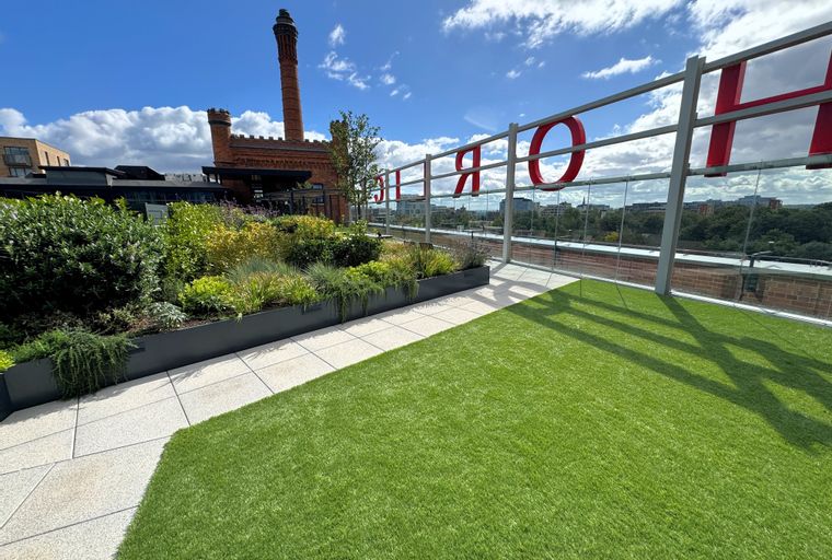 A rooftop terrace with artificial grass, planters, and a city view.