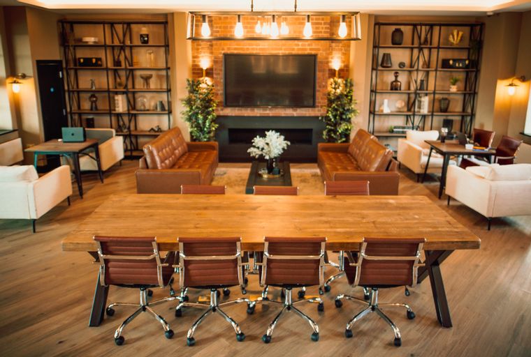 A lounge area with a large wooden table, leather sofas, armchairs, and a television.