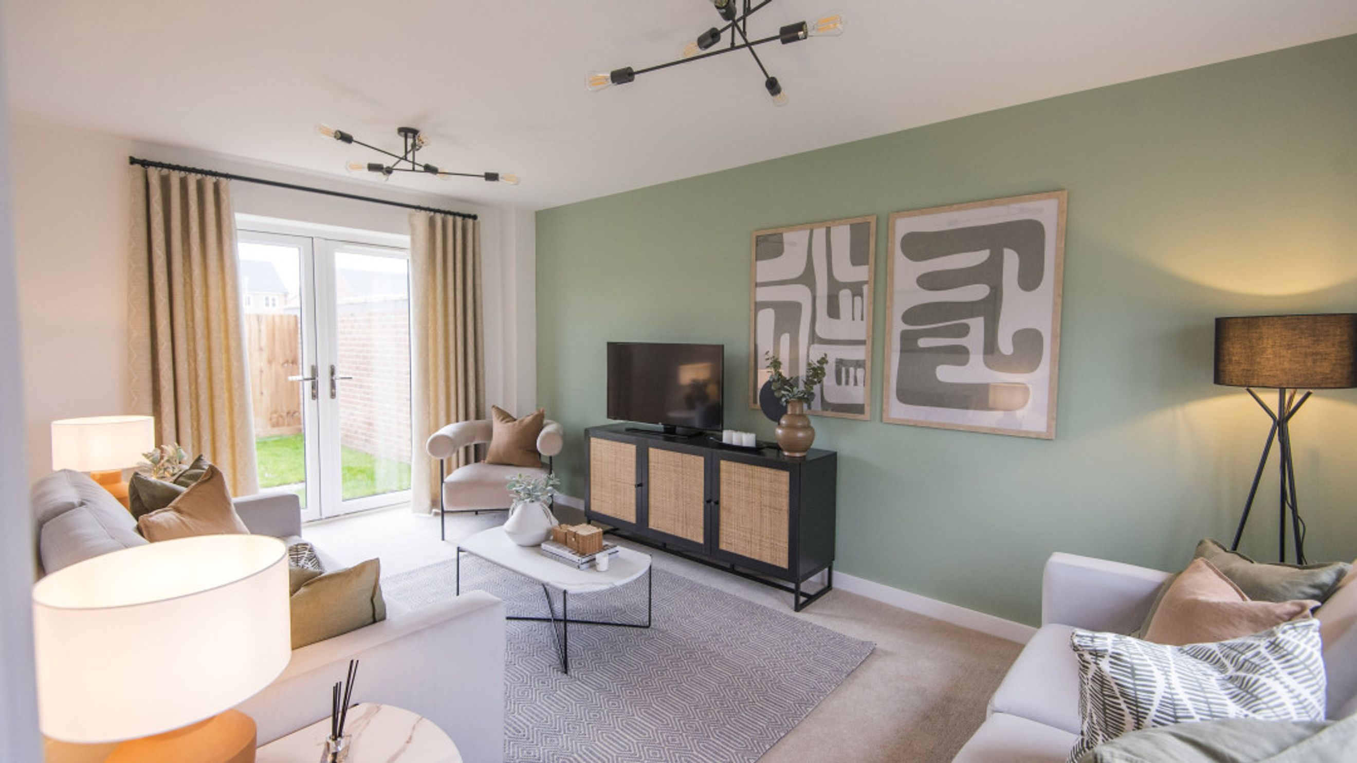 A living room with a television, media console, coffee table, sofas, armchair, and double doors leading to a garden.