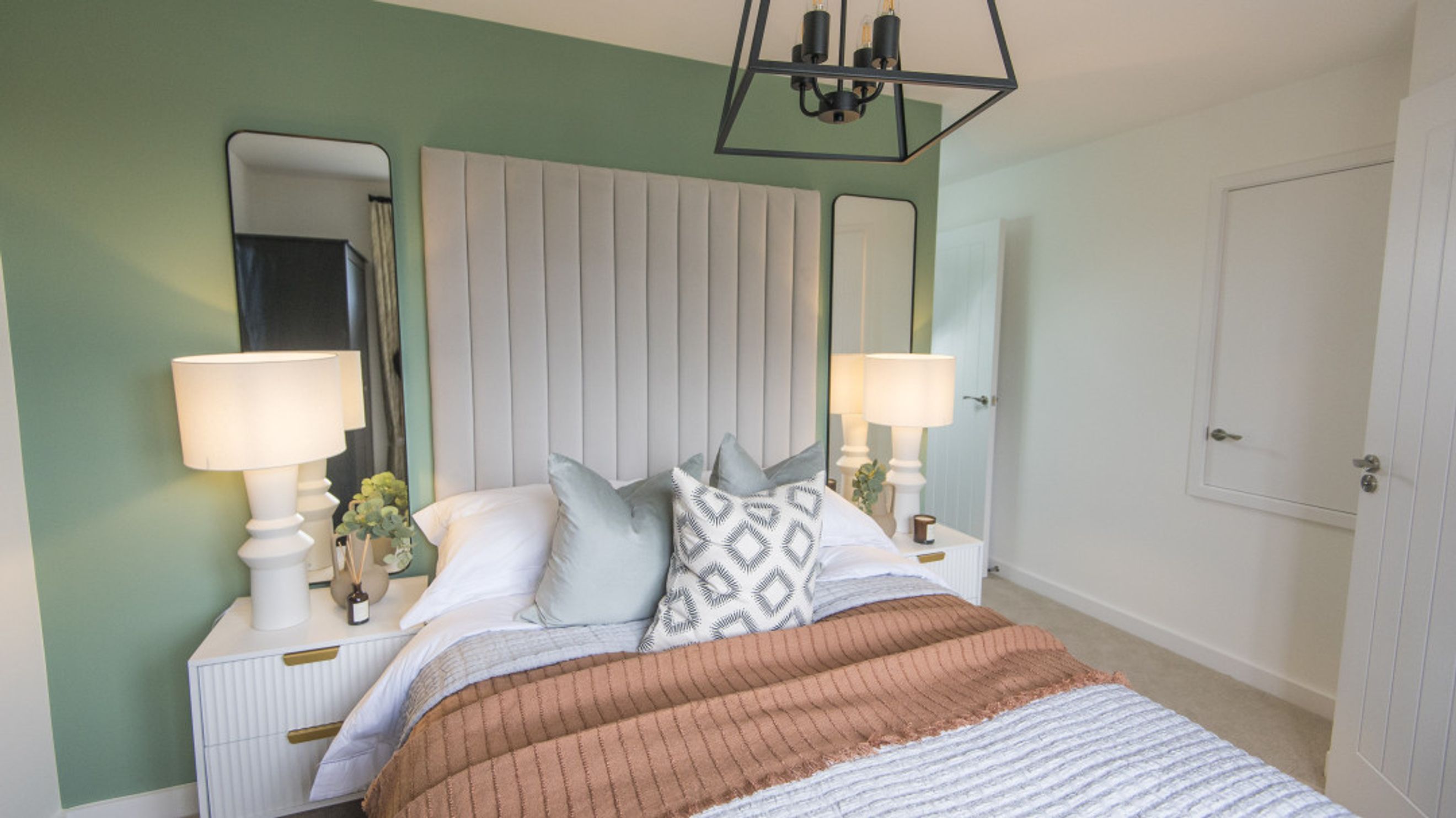 A bedroom with a bed, bedside tables, lamps, and mirrors.