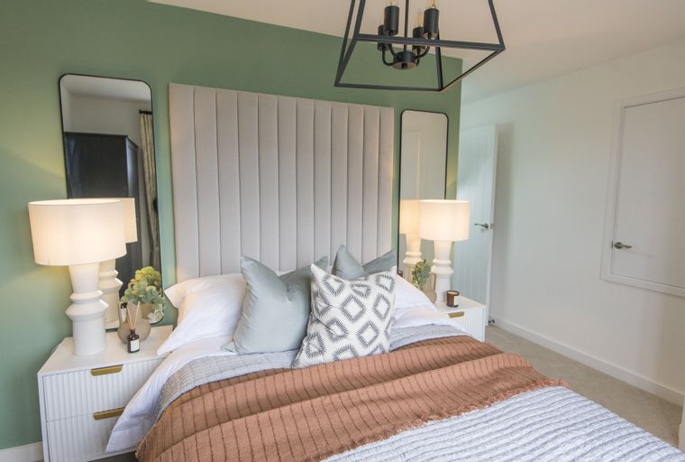 A bedroom with a bed, bedside tables, lamps, and mirrors.