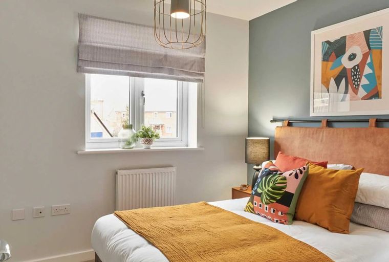 A bedroom with a bed, pillows, a throw blanket, a window, and a piece of art.